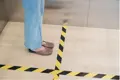 Yellow and Black striped self adhesive tape stuck to floor with a person standing next to.