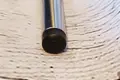 Angled top-down view of a round black heavy duty injection-moulded plastic foot insert fitted to the end of a metal tube leg.