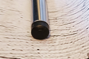 Angled top-down view of a round black heavy duty injection-moulded plastic foot insert fitted to the end of a metal tube leg.