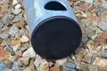A round steel tube with a black plastic tube insert fitted in the end. Laying on gravel.