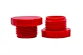 Two red plastic BSP threaded plugs. Both standing on opposite ends.