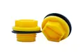 Two Yellow plastic BSP threaded plugs with rubber sealing washers. One standing, one on its side.