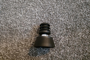 A black plastic round tube insert with threaded hole. With an adjustable foot attached.