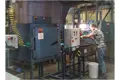 Operator hand dipping PVC parts into a tank between two large ovens producing vinyl components.