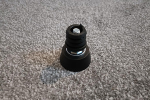 Angled view of A black plastic round tube insert with threaded hole. With an adjustable foot attached.