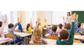 Young students with hands raised in a school classroom, colourful clothing.
