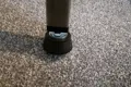 A black plastic threaded square tube insert with an adjustable foot attached. Fitted into a square metal tube. Standing up.