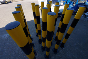 Sixteen Black and Yellow round bollards, with a black tube insert in the end, standing in a car park.